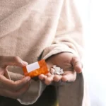 addiction treatment programs covered by insurance - man's hand with pills spilled out of the container .