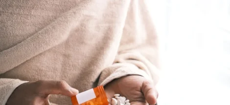 addiction treatment programs covered by insurance - man's hand with pills spilled out of the container .