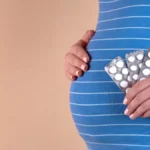 fertility treatment options insurance coverage - A close-up view of the belly of a pregnant woman in a blue T-shirt, which holds pills in her hands. The concept of medicine during pregnancy