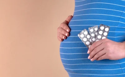 fertility treatment options insurance coverage - A close-up view of the belly of a pregnant woman in a blue T-shirt, which holds pills in her hands. The concept of medicine during pregnancy