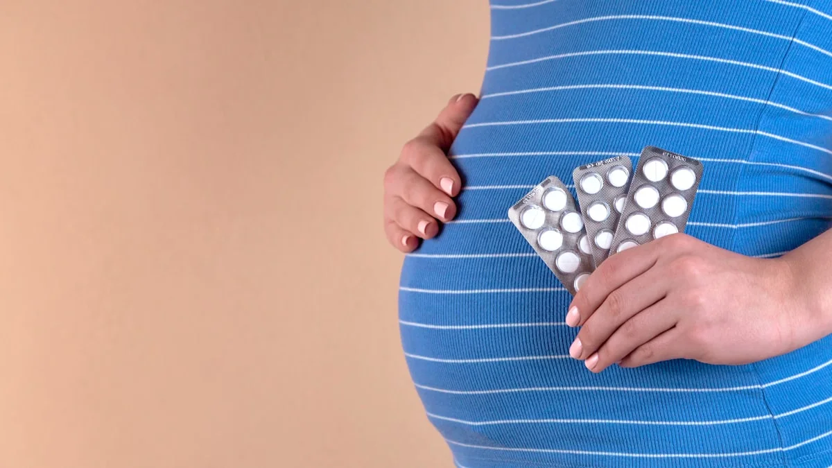 fertility treatment options insurance coverage - A close-up view of the belly of a pregnant woman in a blue T-shirt, which holds pills in her hands. The concept of medicine during pregnancy