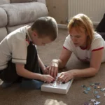 tips for remote learning with children at home US - Young boy assembling a colourful jigsaw puzzle on the carpet with his mother at home
