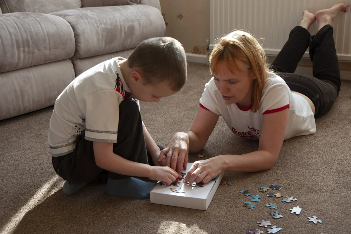 tips for remote learning with children at home US - Young boy assembling a colourful jigsaw puzzle on the carpet with his mother at home